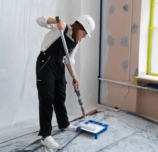 Malerin mit Schutzhelm streicht eine Wand mit der Farbrolle